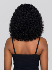 Back view of a person with short, tightly curled black hair wearing a black spaghetti-strap top against a light gray studio background.