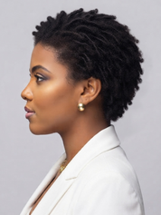 A woman in profile wearing a white blazer and a small gold stud earring, shown against a plain light gray studio background.