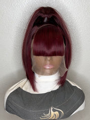 A dark burgundy high-pile wig with matching bangs displayed on a mannequin bust against a textured off-white wall.