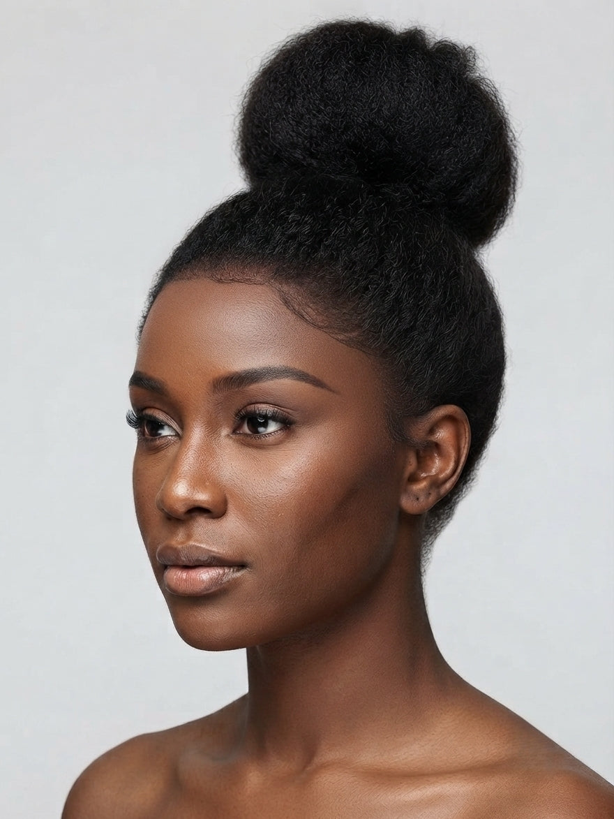 A close-up portrait of a woman with a high, voluminous black hair bun styled in a natural afro texture, shown against a plain light gray background.